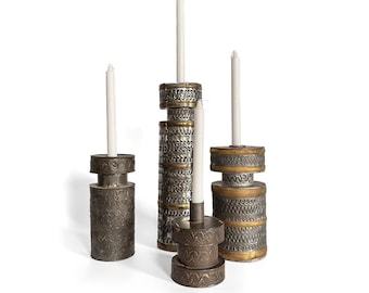 May include: An assortment of decorative metal candle holders in various sizes and designs. The candle holders are silver and gold with intricate patterns, and each holds a white candle. The arrangement is set against a white background.