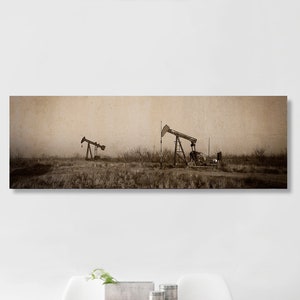 May include: A panoramic photograph of two oil derricks in a field, with a vintage, faded look. The derricks are silhouetted against a hazy sky, with a brown and beige color scheme.