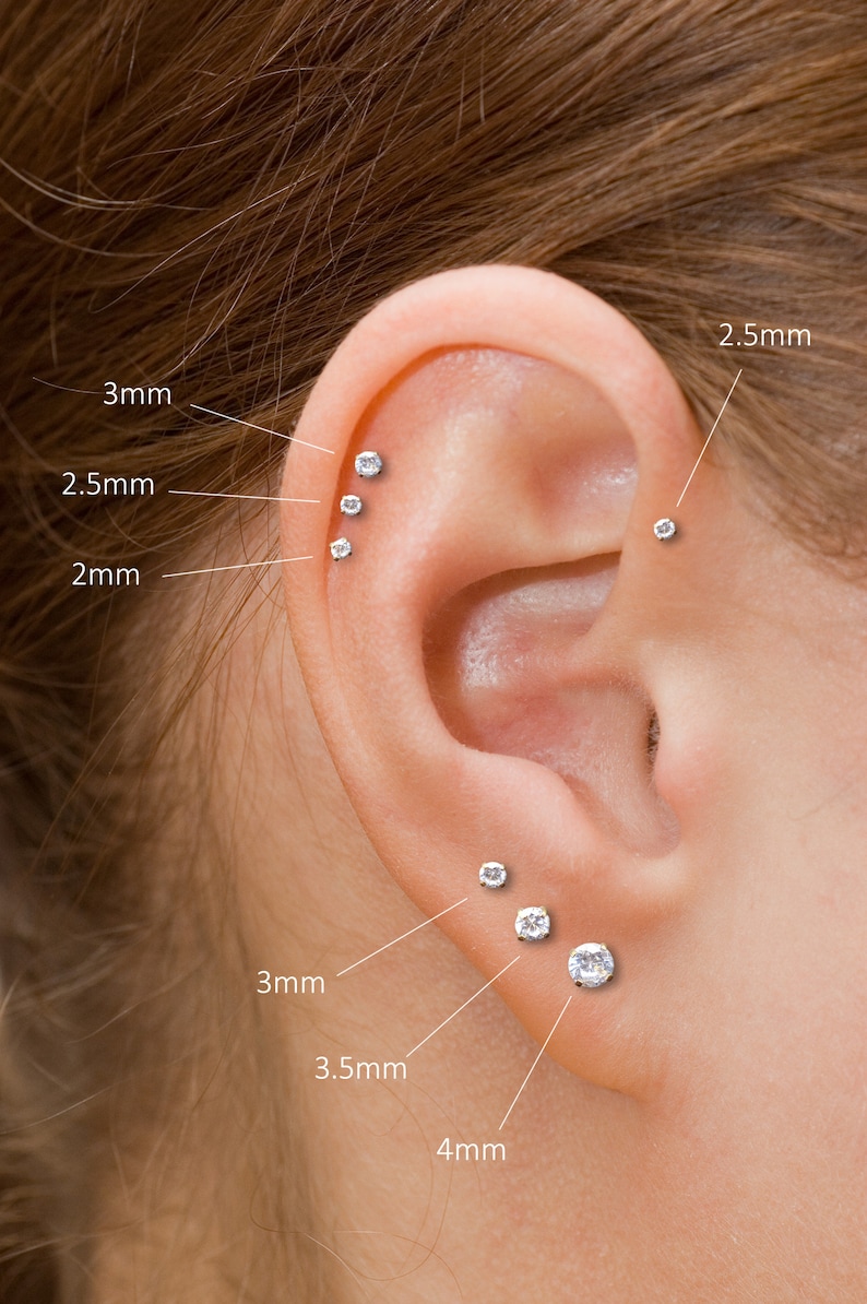 K&ouml;nnte beinhalten: Nahaufnahme eines Ohrs mit mehreren kleinen, runden, durchsichtigen Ohrsteckern. Gr&ouml;&szlig;en sind angegeben: 2 mm, 2,5 mm, 3 mm, 3,5 mm und 4 mm. Das Ohr vor unscharfem Hintergrund.