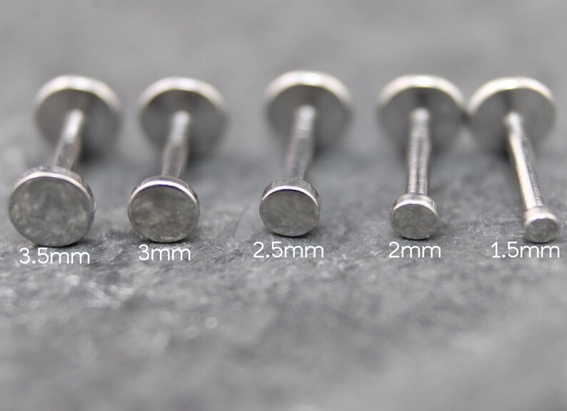 May include: Five silver-toned metal labret studs with flat circular tops arranged in a row. The sizes are labeled below each stud as 3.5mm, 3mm, 2.5mm, 2mm, and 1.5mm, indicating the diameter of the flat circular top of each individual stud.