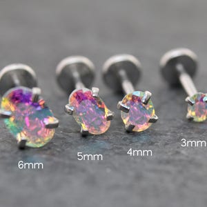 May include: Four iridescent oval-shaped stud earrings in sizes 3mm, 4mm, 5mm, and 6mm. The earrings have a silver-colored post and a prong setting. The iridescent stones reflect a range of colors, including purple, green, and yellow.