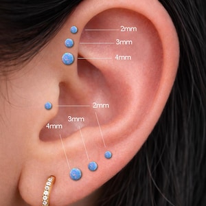 May include: Close-up of an ear with multiple blue opal stud earrings in various sizes: 2mm, 3mm, and 4mm. A gold hoop earring is in the lobe. The image shows the placement of the earrings on the ear.