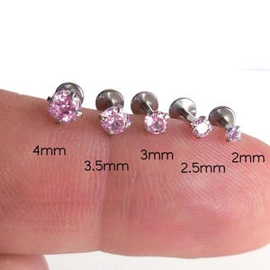 May include: A collection of five pink gemstone stud earrings in varying sizes, ranging from 2mm to 4mm. The earrings are set on silver posts and displayed on a finger. The sizes are labeled in millimeters.