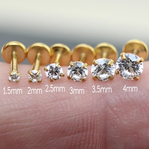 May include: A collection of gold-colored stud earrings with clear, round cubic zirconia stones. Sizes range from 1.5mm to 4mm, labeled on the image. The earrings are displayed on a skin-toned background.