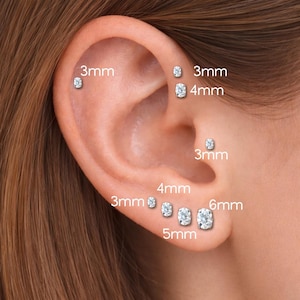 May include: An ear with multiple clear, sparkling stud earrings of varying sizes, ranging from 3mm to 6mm. The earrings are displayed on the ear, with size labels next to each stud.