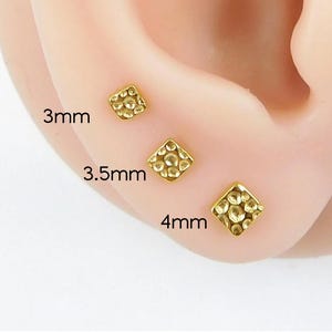 May include: Three gold-colored, square-shaped stud earrings with a textured surface are displayed on an ear. The earrings are 3mm, 3.5mm, and 4mm in size. The sizes are labeled in black text.