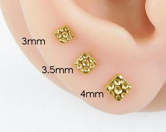 Puede incluir: Tres pendientes de botón cuadrados dorados con una superficie texturizada se muestran en una oreja. Los pendientes miden 3 mm, 3,5 mm y 4 mm. Los tamaños están etiquetados en texto negro.