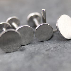 May include: A collection of silver-toned metal labret studs featuring flat, circular discs. Each piece consists of a smooth, round front face attached to a straight, hollow post with a flat circular backing, designed for body piercing applications.