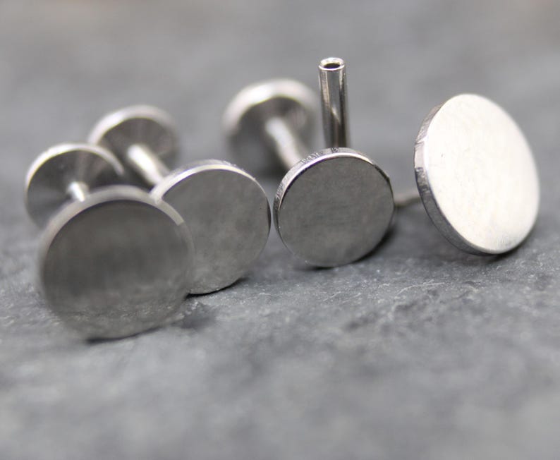 May include: A collection of silver-toned metal labret studs featuring flat, circular discs. Each piece consists of a smooth, round front face attached to a straight, hollow post with a flat circular backing, designed for body piercing applications.