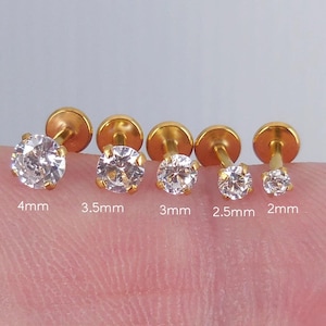 Peut inclure: Cinq boucles d'oreilles à clous dorées avec des pierres précieuses rondes et transparentes de différentes tailles. Les pierres précieuses mesurent 4 mm, 3,5 mm, 3 mm, 2,5 mm et 2 mm de diamètre.