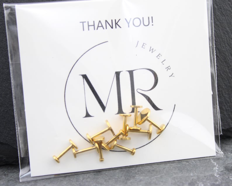 May include: A collection of gold-colored metal labret studs with flat back discs, packaged in a clear plastic sleeve against a white display card featuring the black text THANK YOU! and the logo MR JEWELRY in a circular frame.