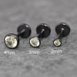 May include: Three black metal stud earrings with clear round faceted stones, arranged by size. The studs are labeled 4mm, 3mm, and 2mm, showing the diameter of each stone. Each earring features a flat circular back and a straight post.