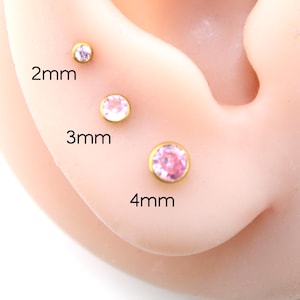 May include: Three gold-tone stud earrings with pink circular stones, labeled with sizes 2mm, 3mm, and 4mm. The earrings are arranged in a vertical line, each featuring a metallic gold setting surrounding a faceted pink gemstone center.
