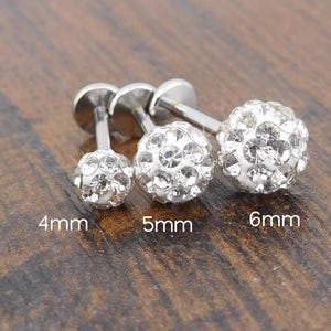 May include: Three silver-colored stud earrings with crystal-like embellishments. The earrings are in three sizes: 4mm, 5mm, and 6mm. The earrings have a round, ball-like design with a flat backing.