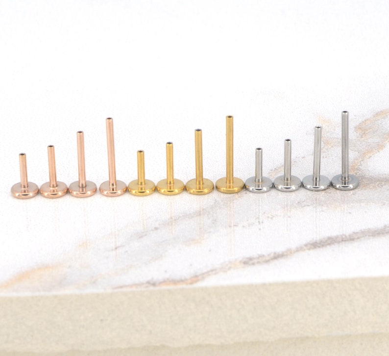 May include: A set of ten surgical steel body jewelry pieces in different lengths. The pieces are in three colors: silver, gold, and rose gold. The jewelry is arranged in order of size, with the smallest piece on the left and the largest piece on the right.