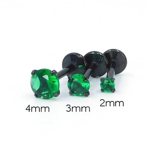 May include: Three black stud earrings with round, emerald green gemstones. The sizes are 4mm, 3mm, and 2mm. The earrings have a flat back and a post for piercing.