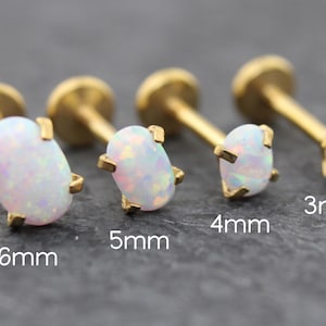 May include: Four gold-colored labret studs with white opal stones. The studs are 3mm, 4mm, 5mm, and 6mm in size. The opal stones have a pearlescent, iridescent quality.