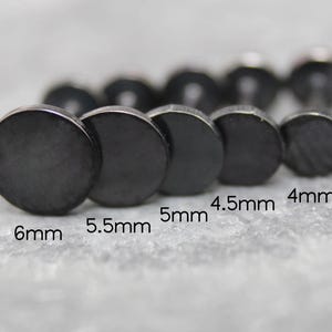 May include: A set of five black circular stud earrings arranged in a row by size. The flat-faced studs are labeled with their respective diameters: 6mm, 5.5mm, 5mm, 4.5mm, and 4mm. Each earring features a smooth, dark metallic finish and a post back.