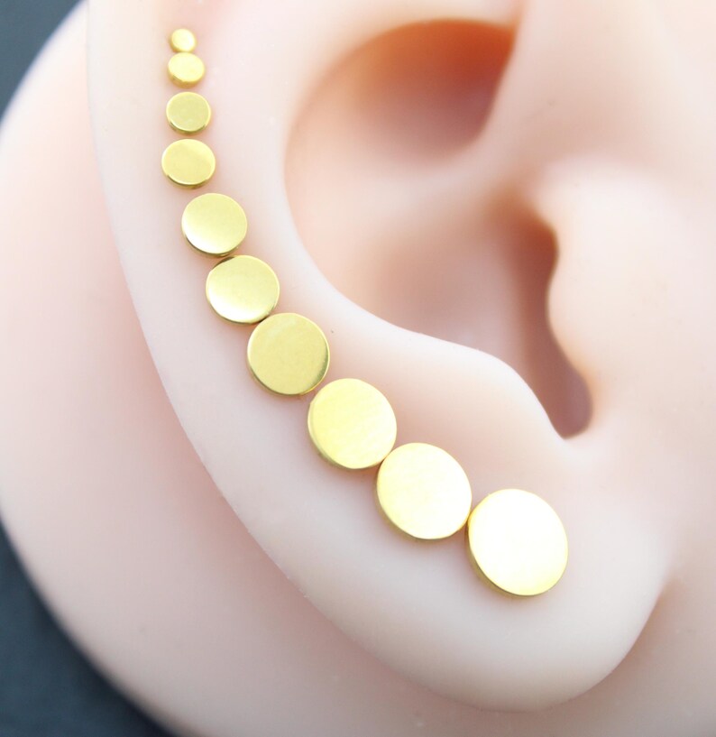 May include: A gold-toned ear climber earring featuring a series of nine circular discs that gradually increase in size from the top to the bottom, following the natural curve of the ear cartilage in a smooth, polished, and metallic finish.