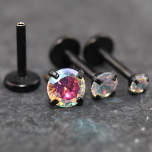 May include: A set of black labret body jewelry pieces featuring round, prong-set iridescent stones that display shifting colors including pink and white. Each piece has a flat circular back and a straight post, designed for piercings.