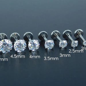 K&ouml;nnte beinhalten: Sechs silberfarbene Labret-Ohrstecker mit klaren, runden Zirkonia-Steinen. Gr&ouml;&szlig;en von 2 mm bis 5 mm. Die Ohrstecker werden vor einem dunklen Hintergrund pr&auml;sentiert.