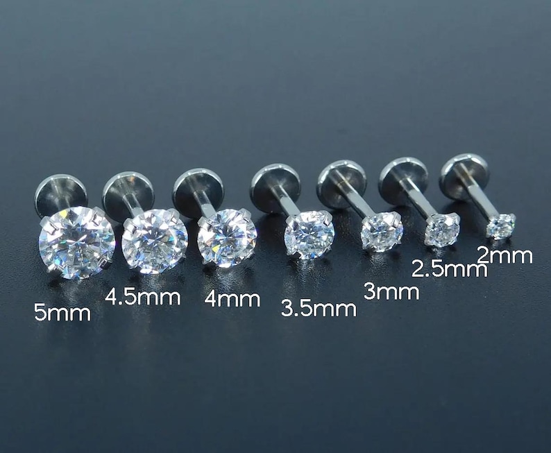 K&ouml;nnte beinhalten: Sechs silberfarbene Labret-Ohrstecker mit klaren, runden Zirkonia-Steinen. Gr&ouml;&szlig;en von 2 mm bis 5 mm. Die Ohrstecker werden vor einem dunklen Hintergrund pr&auml;sentiert.