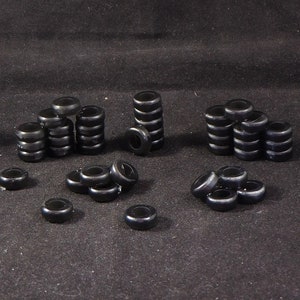 May include: A collection of black rubber tire-shaped toy pieces stacked in various heights. Some pieces are arranged in small piles, while others are stacked in tall columns.