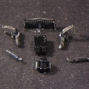 May include: A set of black plastic model car parts, including a grill, engine, exhaust pipes, and two side pieces.