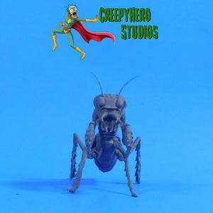 May include: A gray insect-like figurine with multiple legs and antennae, set against a blue background. The figurine has a detailed, menacing face. Above it, the text "CREEPYHERO STUDIOS" is displayed, along with a cartoon character.