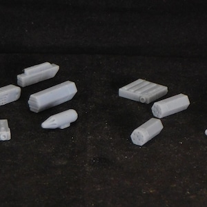 May include: A collection of gray plastic model parts for a miniature spaceship or aircraft. The parts include various shapes and sizes, such as cylinders, cones, and rectangular blocks.