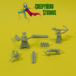 May include: A set of grey plastic miniature figures and weapons, including a crossbow, a catapult, and several soldiers. The figures are posed in various action poses. The set is labeled "CreepyHero Studios".