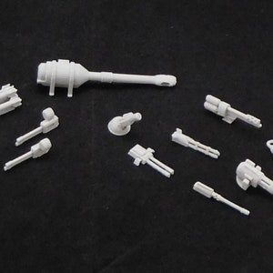 May include: A set of 11 white plastic model parts for a spaceship or aircraft. The parts include a large cannon, several smaller cannons, and a variety of missile pods.