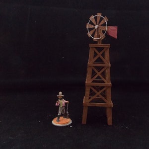 May include: A miniature wooden windmill with a red flag and a brown wooden base. A miniature figure of a person with a hat and a stick is standing in front of the windmill.