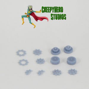 May include: A set of 11 gray plastic gears, including 6 small gears and 5 larger gears. The gears are arranged in a pattern on a white surface.
