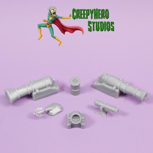 May include: A set of six grey plastic miniature cannons, including a small cannon, a larger cannon, a barrel, and two cannons with bases. The cannons are all in various stages of assembly.