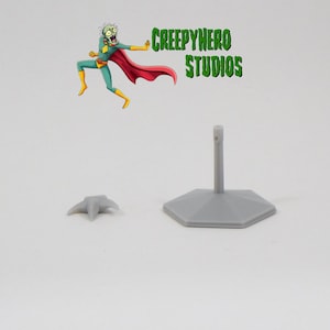 May include: A gray plastic base with a hexagonal shape and a tall, thin post. There is a separate gray plastic piece with three points, which appears to be a separate part of the base.