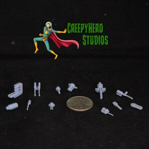 May include: A set of 11 gray plastic model parts for a miniature spaceship or aircraft. The parts are small and detailed, and they are arranged on a black surface. The parts are about the size of a US quarter.