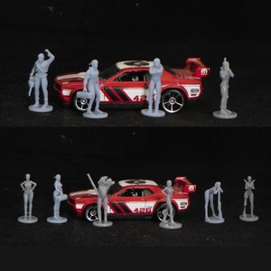 May include: A red Dodge Challenger toy car with gray figures standing around it. The car has black racing stripes and the number 426 on the side.