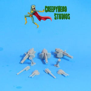 May include: A set of eight grey plastic miniature cannons, some with barrels pointing forward and others with barrels pointing upward. The cannons are on a blue surface.