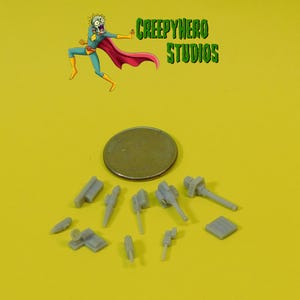 May include: A collection of small, gray, plastic model gun parts, including barrels, turrets, and bases. The parts are arranged on a yellow surface next to a US quarter for scale.