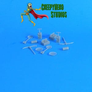 May include: A collection of miniature grey plastic tools, including shovels, pickaxes, and a pan, on a blue background. The tools are part of a set of miniature props for a tabletop game or diorama.