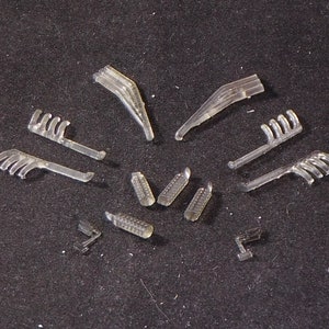 May include: A set of clear plastic model parts for a vehicle. The parts include a variety of shapes, including curved pieces, straight pieces, and pieces with multiple prongs.