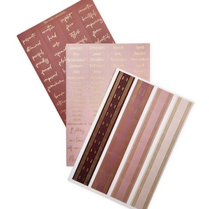 May include: Three sheets of planner stickers in pink and burgundy hues. One sheet has gold text with inspirational words. Another has monthly calendar labels. The third has vertical stripes.