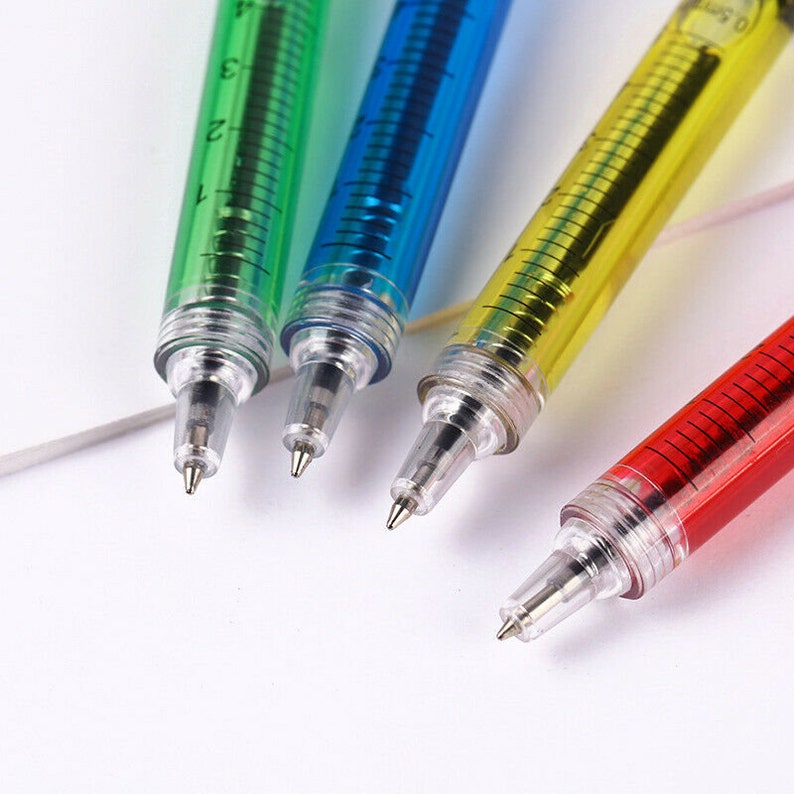 May include: Four colorful syringe-shaped pens with clear plastic barrels and silver tips. The pens are filled with green, blue, yellow, and red liquid.