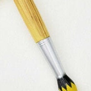 May include: A paintbrush with a wooden handle and a silver ferrule. The bristles are yellow with black accents. The brush is angled against a white background.