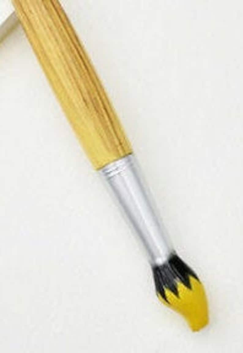 May include: A paintbrush with a wooden handle and a silver ferrule. The bristles are yellow with black accents. The brush is angled against a white background.