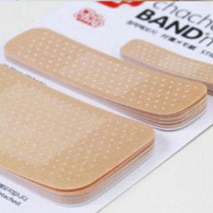 May include: A pack of adhesive memo notes shaped like band-aids. The notes are beige with a dotted pattern and the text "chachap BANDmemo STICKY MEMOS" is printed on the packaging.