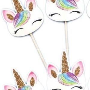 May include: Four white unicorn cupcake toppers with gold glitter horns and rainbow manes. The toppers are on wooden sticks.