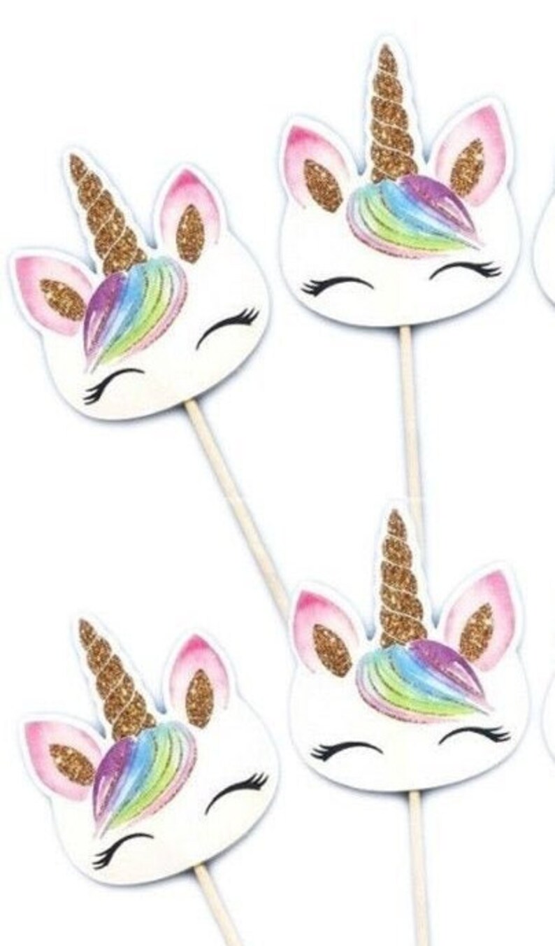 May include: Four white unicorn cupcake toppers with gold glitter horns and rainbow manes. The toppers are on wooden sticks.