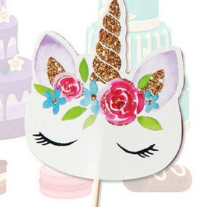 May include: A white unicorn cake topper with a gold glitter horn, pink and blue flowers, and closed eyes. The unicorn is holding a stick.